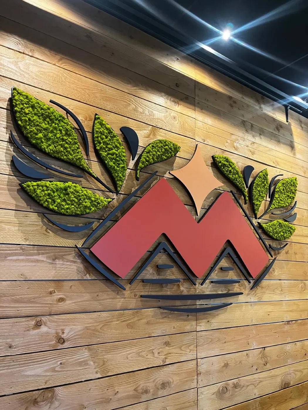 Gros plan du logo mural en relief : M rouge, étoile saumon et feuilles en lichen stabilisé