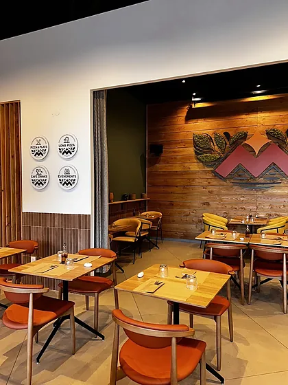 La salle de Lodève : fauteuils moutarde, tables en bois et M rouge végétalisé sur le mur