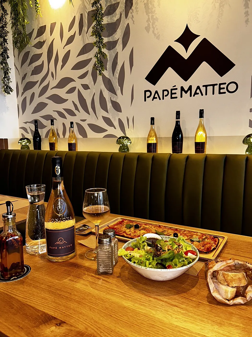 La Long Pizza® sur sa planche avec salade fraîche et vin de la maison, sous le logo mural Papé Matteo
