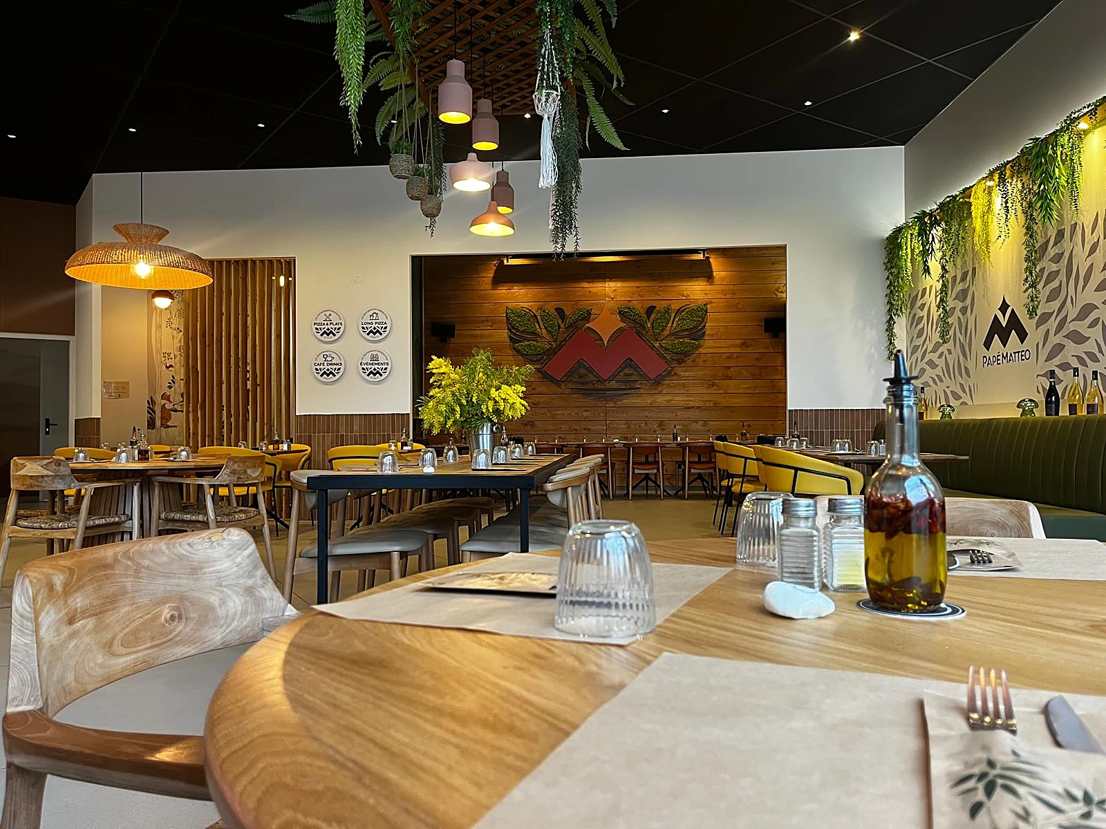 La salle de Lodève en grand : mimosa sur les tables, banquette verte et M en marqueterie au fond